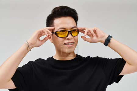 Ein modischer junger Mann in schwarzem Hemd posiert selbstbewusst mit auffälliger gelber Sonnenbrille.