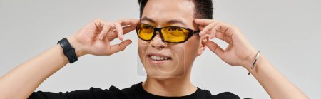 Téléchargez les photos : Un jeune homme à la mode posant activement dans une chemise noire et des lunettes de soleil jaunes, respirant style et confiance. - en image libre de droit