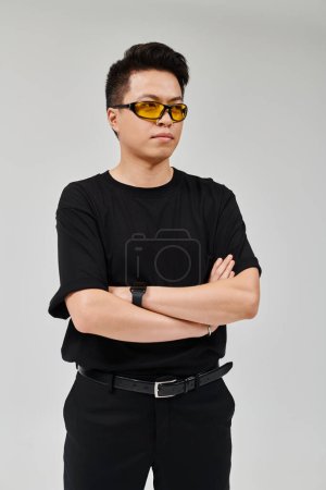 Un jeune homme à la mode pose dans une chemise noire élégante et des lunettes de soleil élégantes.