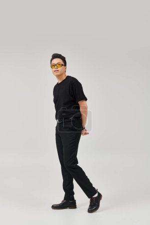 A fashionable young man strikes a pose in a stylish black shirt and trendy sunglasses.