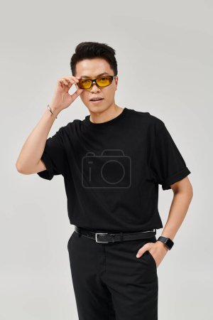 Ein modischer junger Mann in schwarzem Hemd posiert selbstbewusst mit seiner Sonnenbrille.