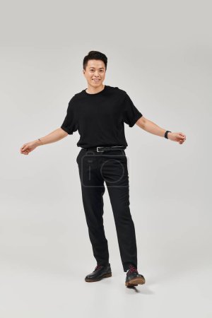 Ein modischer junger Mann in schwarzem Hemd und schwarzer Hose posiert dynamisch in einem eleganten Rahmen.