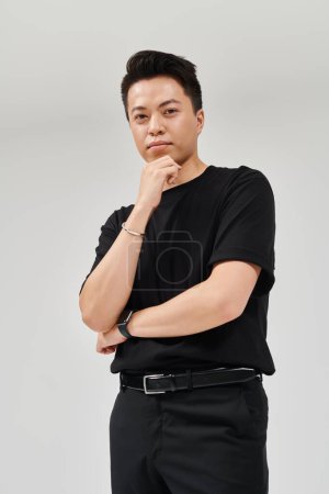 A fashionable young man in a sleek black shirt strikes a captivating pose for a portrait.