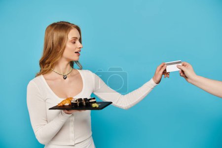 Photo for A blonde woman handing a card to another woman, both engaged in a friendly exchange over delicious Asian cuisine. - Royalty Free Image