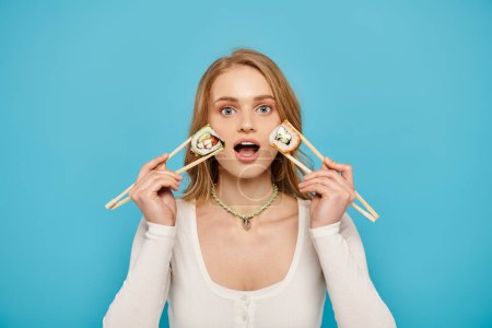 A beautiful woman with blonde hair holding two chopsticks over her eyes in a playful and artistic pose.