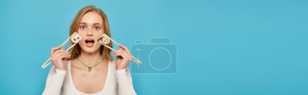 A beautiful woman with blonde hair holds up chopsticks with sushi near her face
