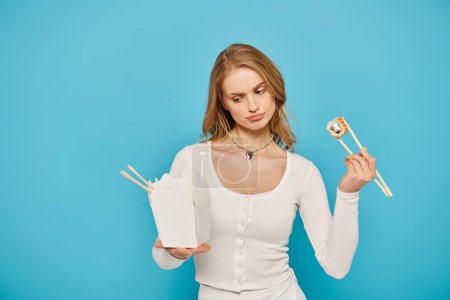 Eine Frau mit blonden Haaren hält Essstäbchen und eine Schachtel mit asiatischem Essen in der Hand