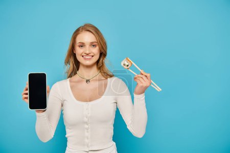 A woman balances a cell phone and chopsticks on blue backdrop