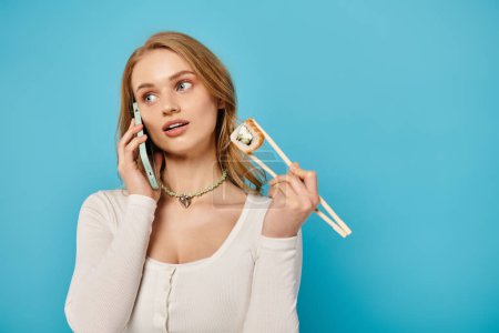 Una mujer elegante sosteniendo palillos y sushi y talkng por teléfono