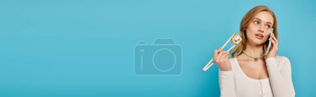 Photo for A trendy woman holding chopsticks and sushi and talking by phone, banner - Royalty Free Image