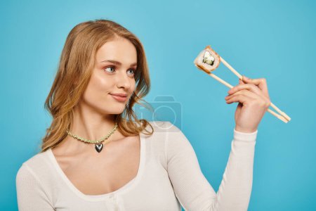 Téléchargez les photos : Une superbe femme blonde tient délicatement une paire de baguettes, mettant en valeur sa grâce et son équilibre. - en image libre de droit