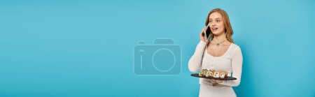 Téléchargez les photos : Une superbe femme blonde tient un plateau de sushi tout en bavardant sur son téléphone portable. - en image libre de droit