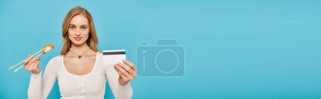 Photo for A beautiful woman with blonde hair holds a credit card and chopsticks with sushi in her hands - Royalty Free Image
