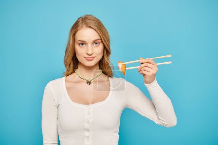 Photo for A blonde woman elegantly holds chopsticks and a delectable piece of Asian cuisine. - Royalty Free Image