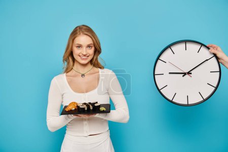 Téléchargez les photos : Une femme blonde tenant une assiette de nourriture asiatique devant une horloge. - en image libre de droit