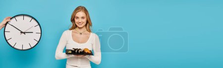 Téléchargez les photos : Une femme élégante aux cheveux blonds se tient à côté d'une horloge, tenant un plateau de nourriture asiatique délicieuse. - en image libre de droit
