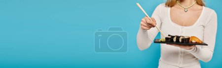 Photo for Cropped view of woman elegantly holding chopsticks and a plate of sushi. - Royalty Free Image