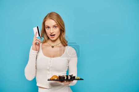 Téléchargez les photos : Une femme élégante tenant une assiette de cuisine asiatique et une carte de crédit avec une expression confiante. - en image libre de droit