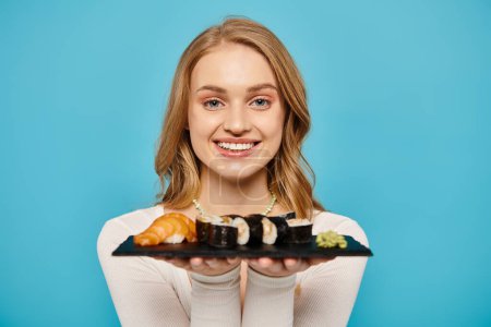 A beautiful blonde woman delicately holds a plate of freshly prepared sushi.