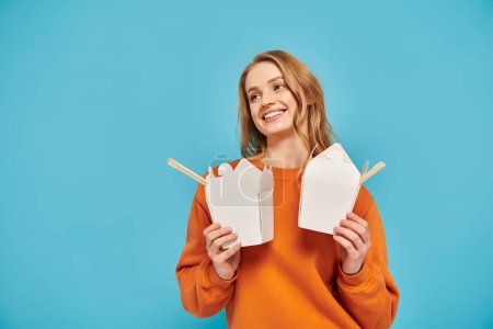 A woman with blonde hair holding two boxes of Asian food in front of her face.