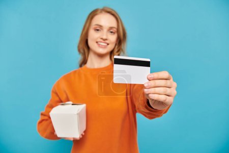 A stylish woman holds a credit card and a box, showcasing a modern lifestyle and consumerism.