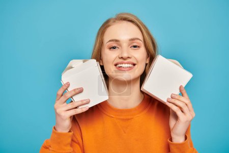 A woman with blonde hair holds two boxes in front of her face, showcasing delicious Asian food.