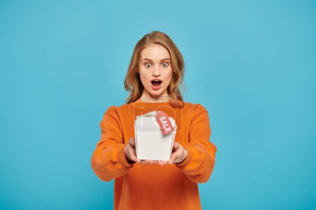 A beautiful blonde woman holding a food box, looking surprised.