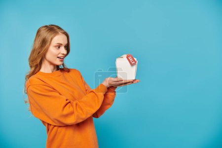 Photo for A blonde woman in an orange shirt holds a food box containing delicious Asian cuisine. - Royalty Free Image
