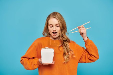Photo for A beautiful blonde woman holds a box of noodles and chopsticks, exuding elegance and enjoying Asian cuisine. - Royalty Free Image