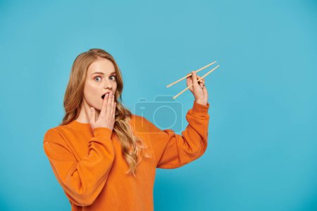 A stylish woman in an orange sweater gracefully holds a pair of chopsticks, ready to enjoy Asian cuisine.