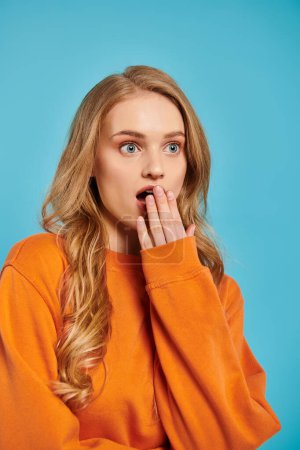 A blonde woman looks surprised on bright blue backdrop.