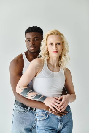 Téléchargez les photos : Un jeune couple multiculturel côte à côte dans un studio sur fond gris. - en image libre de droit