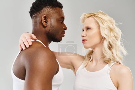 Ein junges multikulturelles Paar steht eng beieinander in einem Atelier vor grauem Hintergrund.