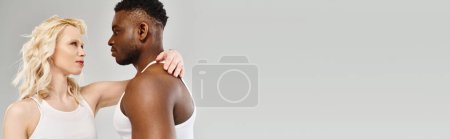 Photo for A young multicultural couple stands side by side in a studio against a grey background, exuding unity and connection. - Royalty Free Image