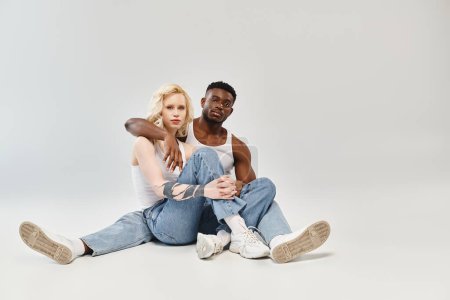 Foto de Un hombre y una mujer jóvenes se sientan de cerca en el suelo, perdidos en la conversación y la conexión contra un fondo gris. - Imagen libre de derechos