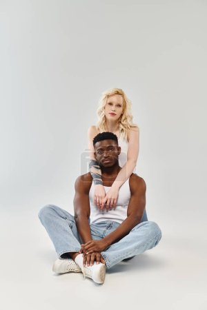 Un homme assis sur le sol soutient une femme sur le dos, montrant sa confiance, son équilibre et sa connexion dans un studio..