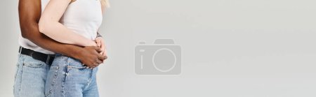 Photo for A young multicultural couple standing side by side in a studio, showcasing unity and togetherness against a grey background. - Royalty Free Image