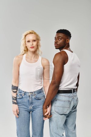 Téléchargez les photos : Un jeune couple multiculturel côte à côte dans un studio sur fond gris. - en image libre de droit
