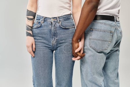 A young multicultural couple standing next to each other in a studio against a grey background.
