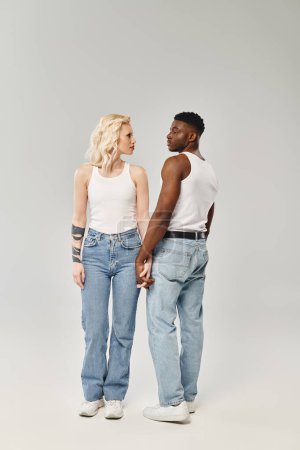 Téléchargez les photos : Un jeune couple multiculturel se tient côte à côte dans un studio sur fond gris, mettant en valeur l'unité et la convivialité. - en image libre de droit