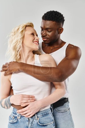 A man and a woman, a young multicultural couple, embracing each other in a warm gesture of love on a grey studio background.