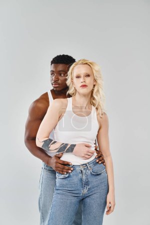 Téléchargez les photos : Un jeune couple interracial se tenant côte à côte dans un studio, respirant l'unité et la connexion dans un contexte gris. - en image libre de droit