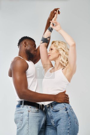 A young interracial couple dancing gracefully together in a studio against a grey background.