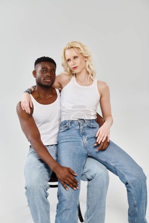 A young interracial couple gracefully seated on a chair in a studio, showcasing unity and love.