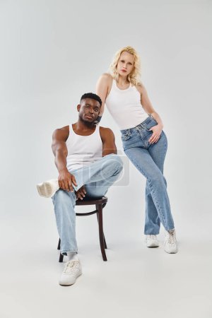 A young man and woman, an interracial couple, striking a pose in a stylish studio setting against a grey backdrop.