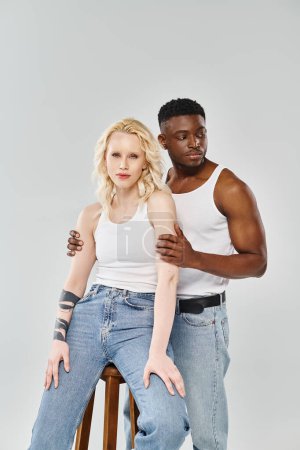 A young interracial couple sitting on a stool in a studio against a grey background.