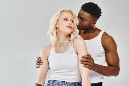 Young interracial couple standing together in a studio against a grey background.