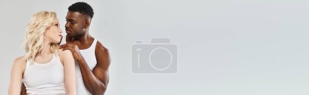 Téléchargez les photos : Un jeune couple interracial debout ensemble dans un studio sur fond gris, mettant en valeur l'unité et la convivialité. - en image libre de droit