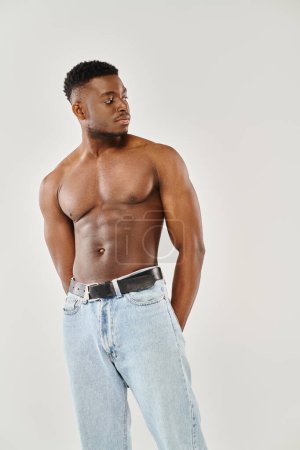 A young, shirtless, African American man confidently posing in a studio against a grey background.
