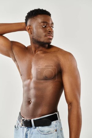 A young, shirtless African American man strikes a captivating pose with his hand resting on his head in a studio against a grey background.